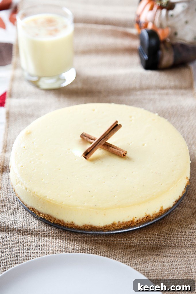 Eggnog Cheesecake Recipe: Creamy Holiday Dessert with Rum Optional 4 a whole eggnog cheesecake garnished 2 cinnamon sticks with a glass of eggnog in the background.