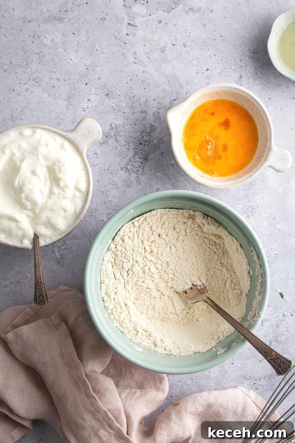 A bowl with flour in it, a bowl with a whisked egg, and a bowl of buttermilk all on a grey counter.