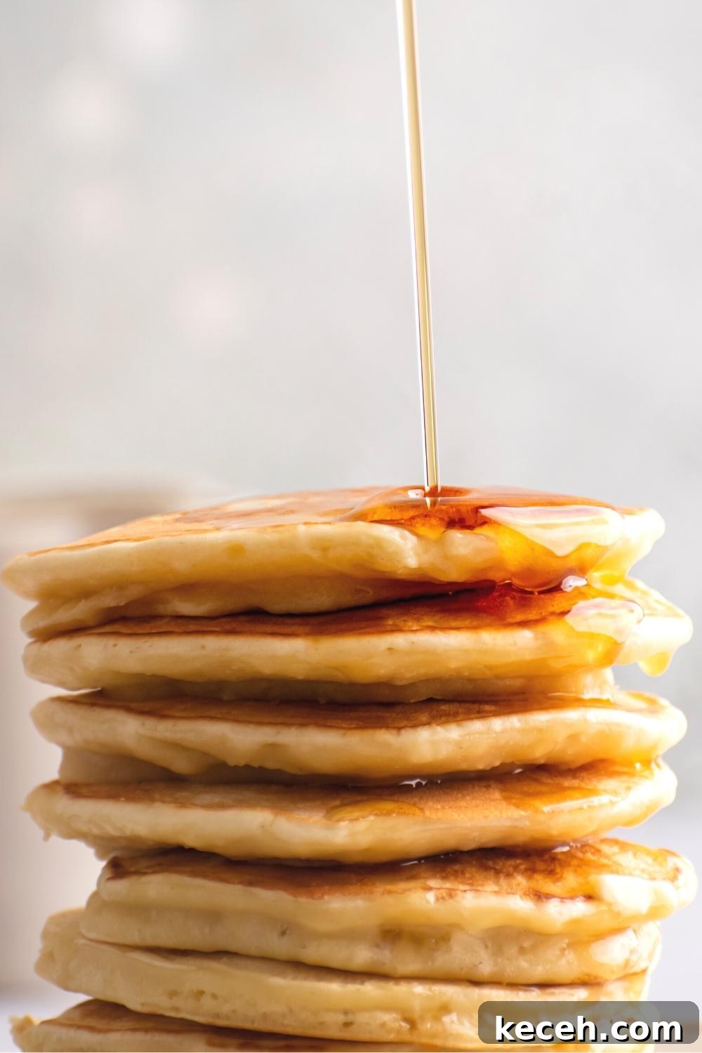 Maple syrup drizzling on top of a stack of six pancakes.