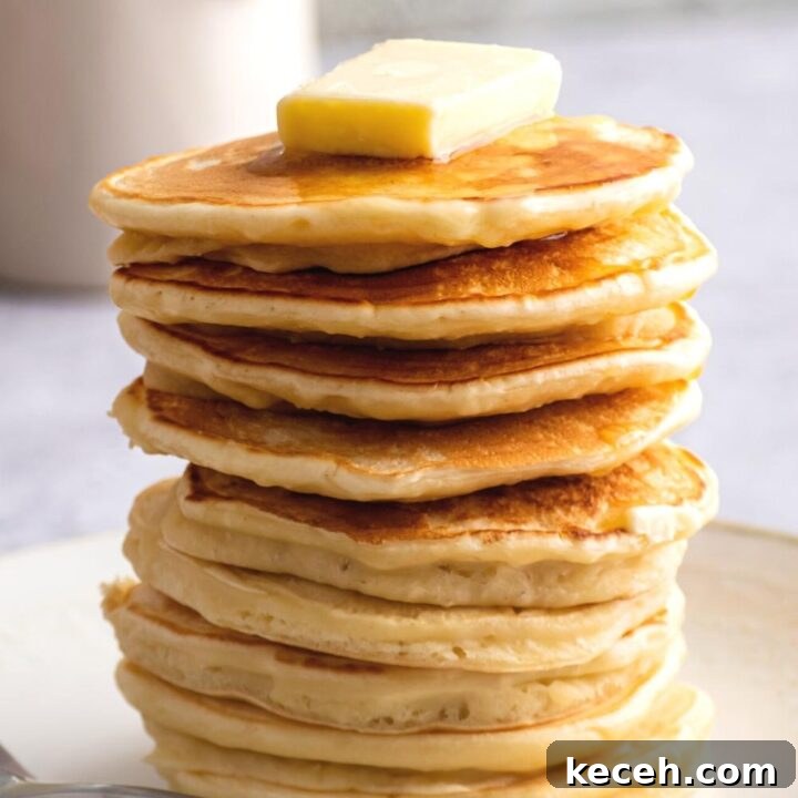 A stack of ten Denny's pancakes with a square of butter on the top pancake.