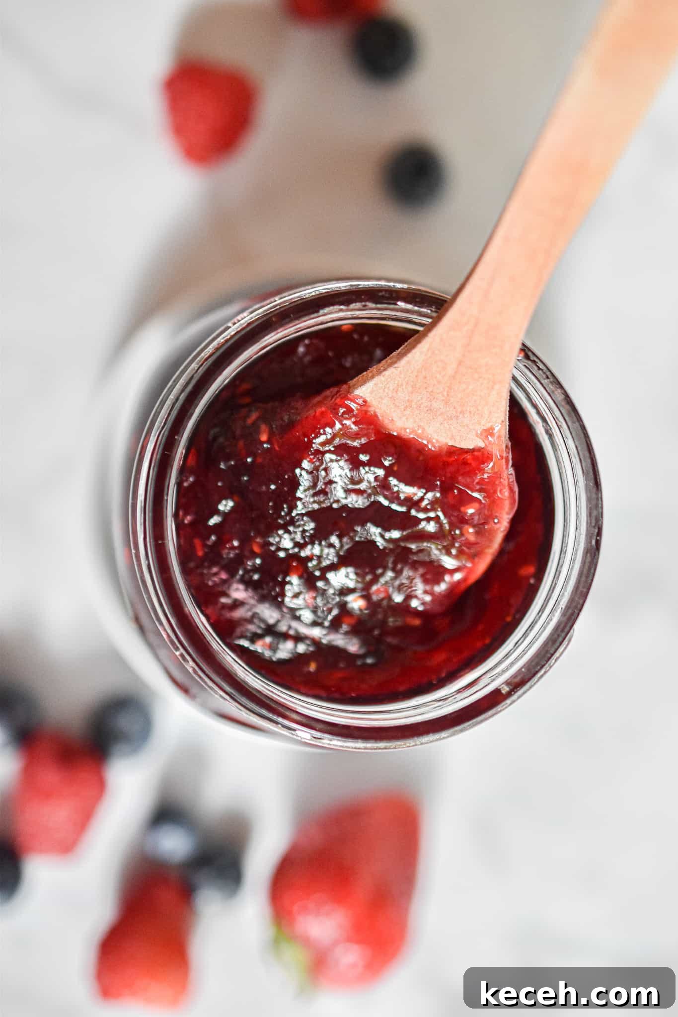 A spoon is lifting the jam out of the jar.