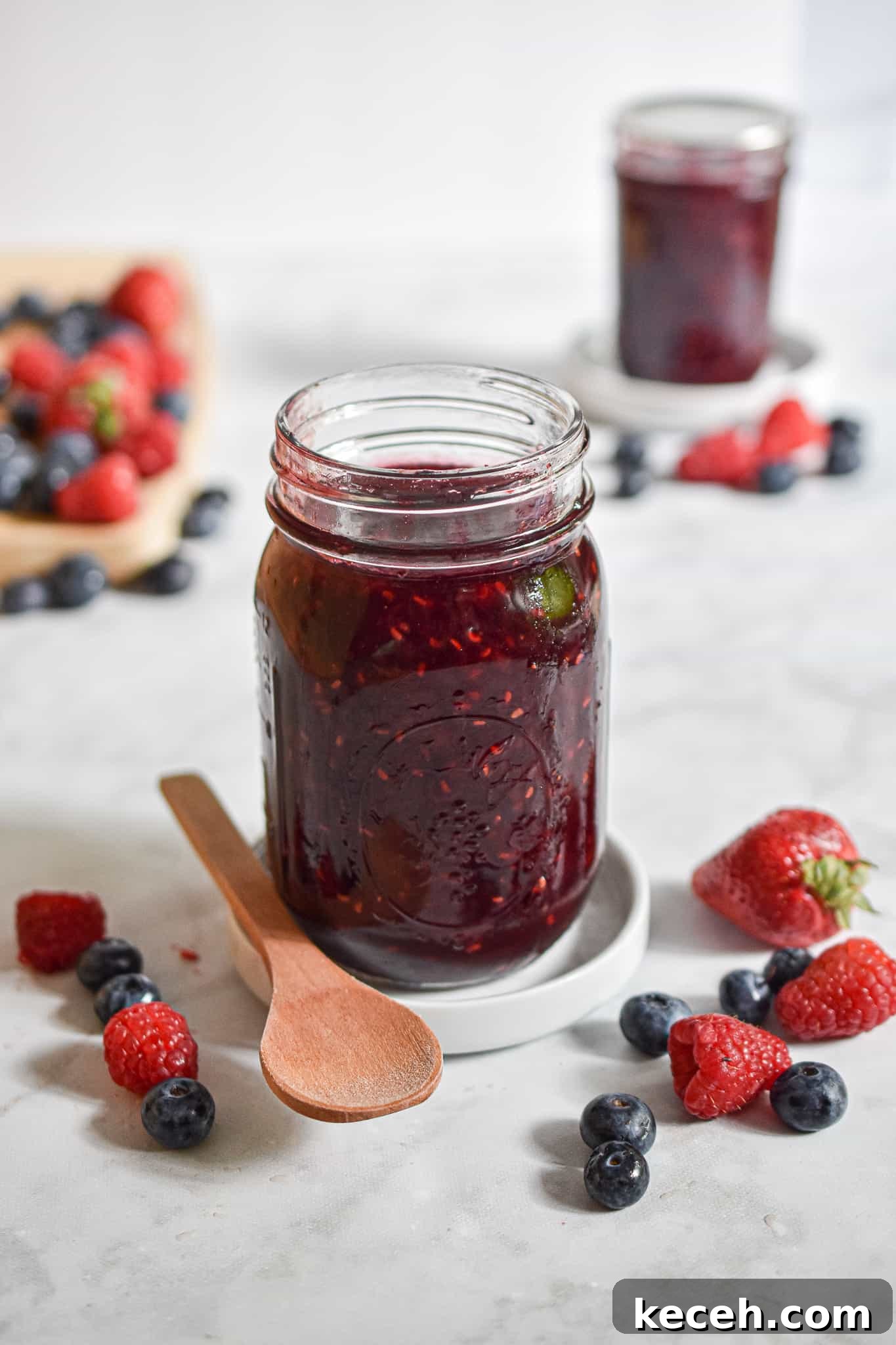 A jar of jam is in front of another jar of jam with fruit around it.