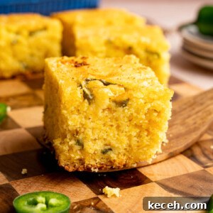 Spicy Jalapeño Cheddar Cornbread Recipe 7 A serving utensil holds a piece of jalapeno cheddar cornbread on top of a wooden cutting board for serving.