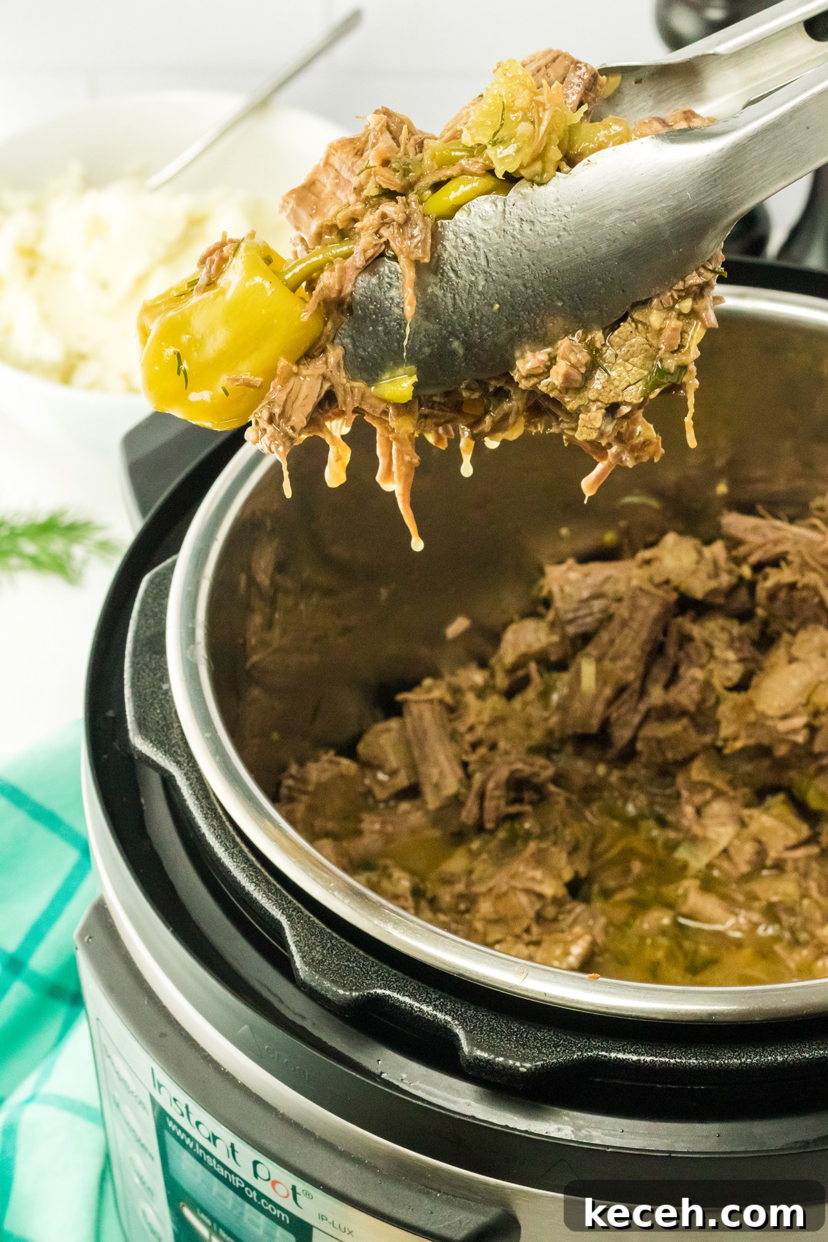 Removing shredded roast beef out of instant pot with tongs.