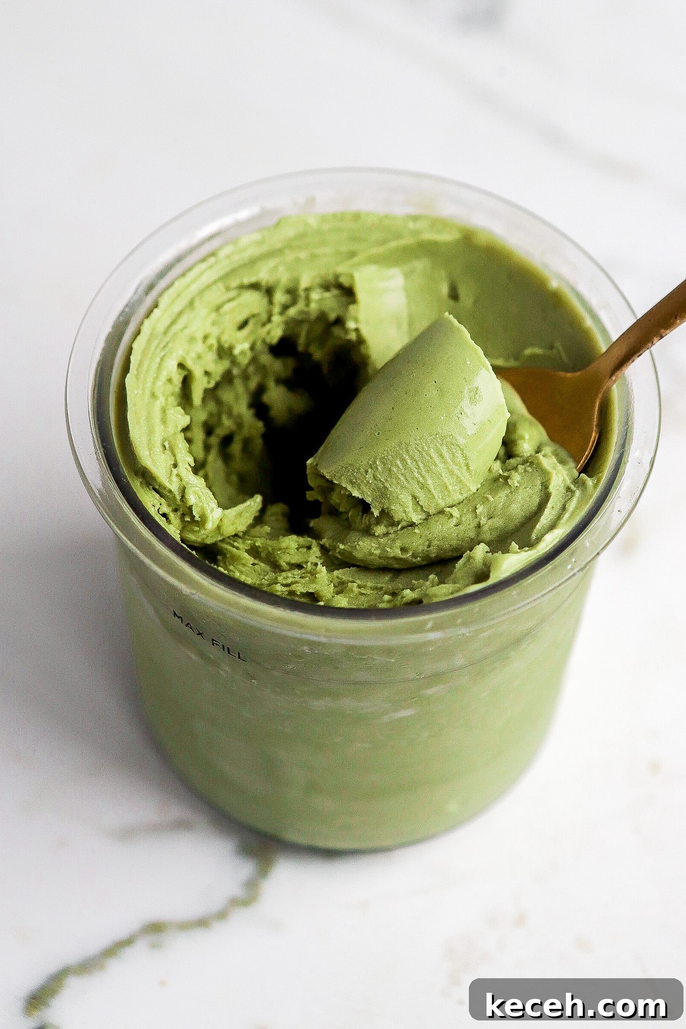 Side view of matcha protein ice cream in ninja creami pint container with gold spoon.