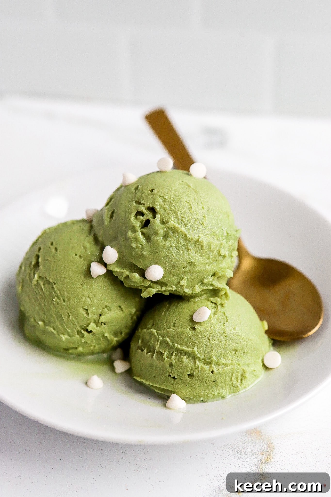 Side angle of matcha dessert in small white bowl with gold spoon.