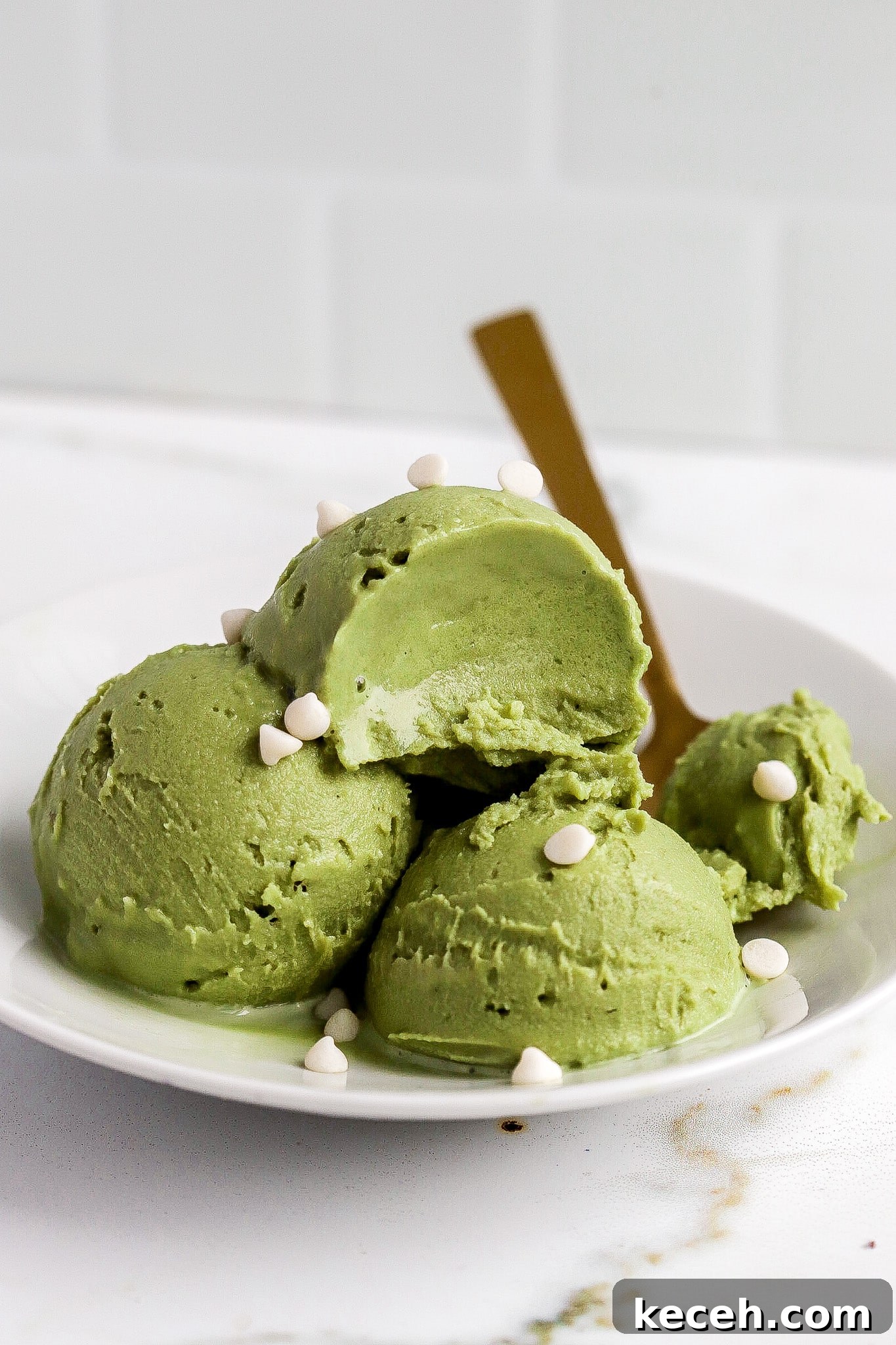 Side view of matcha ice cream scoops in white bowl with gold spoon and mini white chocolate chips.