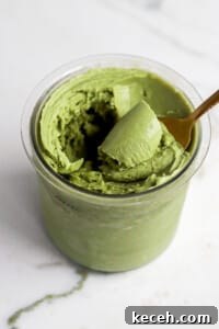 Side view of matcha protein ice cream in ninja creami pint container with gold spoon.