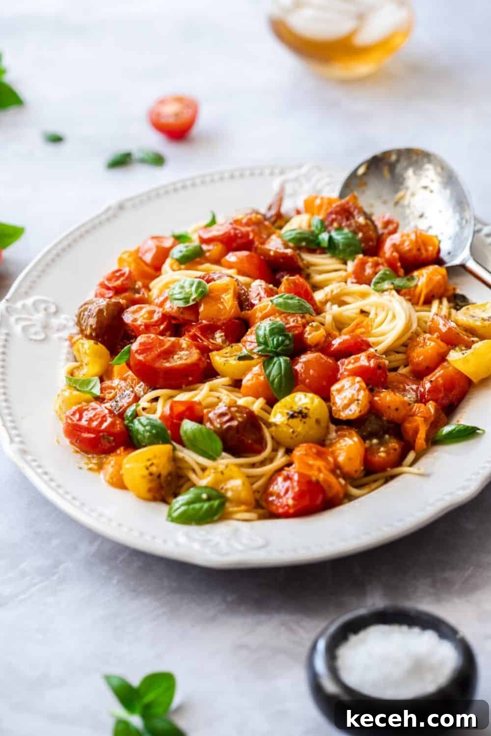 Roasted Cherry Tomato Pasta with Garlic and Basil 5 large white platter of pasta, topped with roasted tomato sauce and garnished with basil leaves. silver spoon on edge of dish.