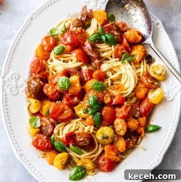 Roasted Cherry Tomato Pasta with Garlic and Basil 6 large white platter of pasta, topped with roasted tomato sauce and garnished with basil leaves. silver spoon on edge of dish.