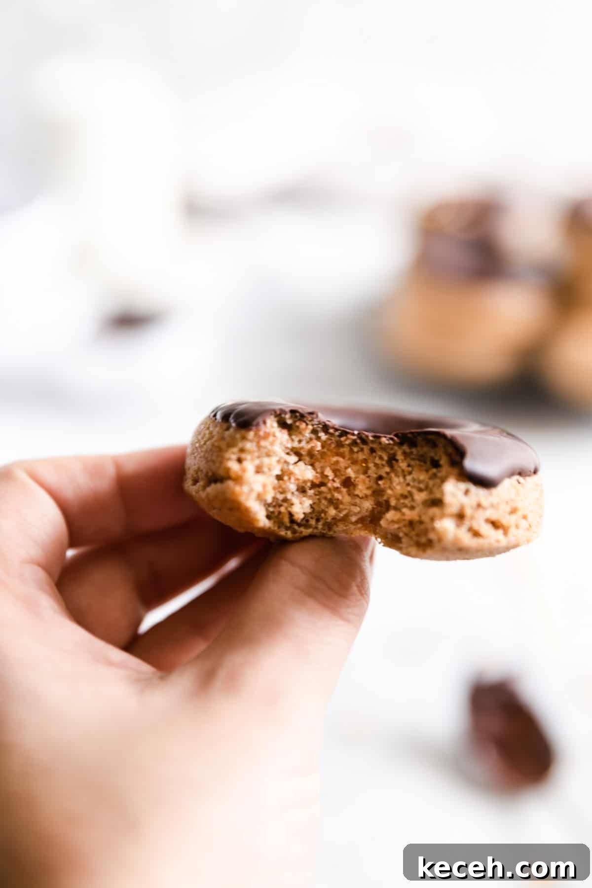 Baked Donuts with Rich Chocolate Glaze Recipe 12 close up of a hand holding a baked doughnut with a small bite taken out of it