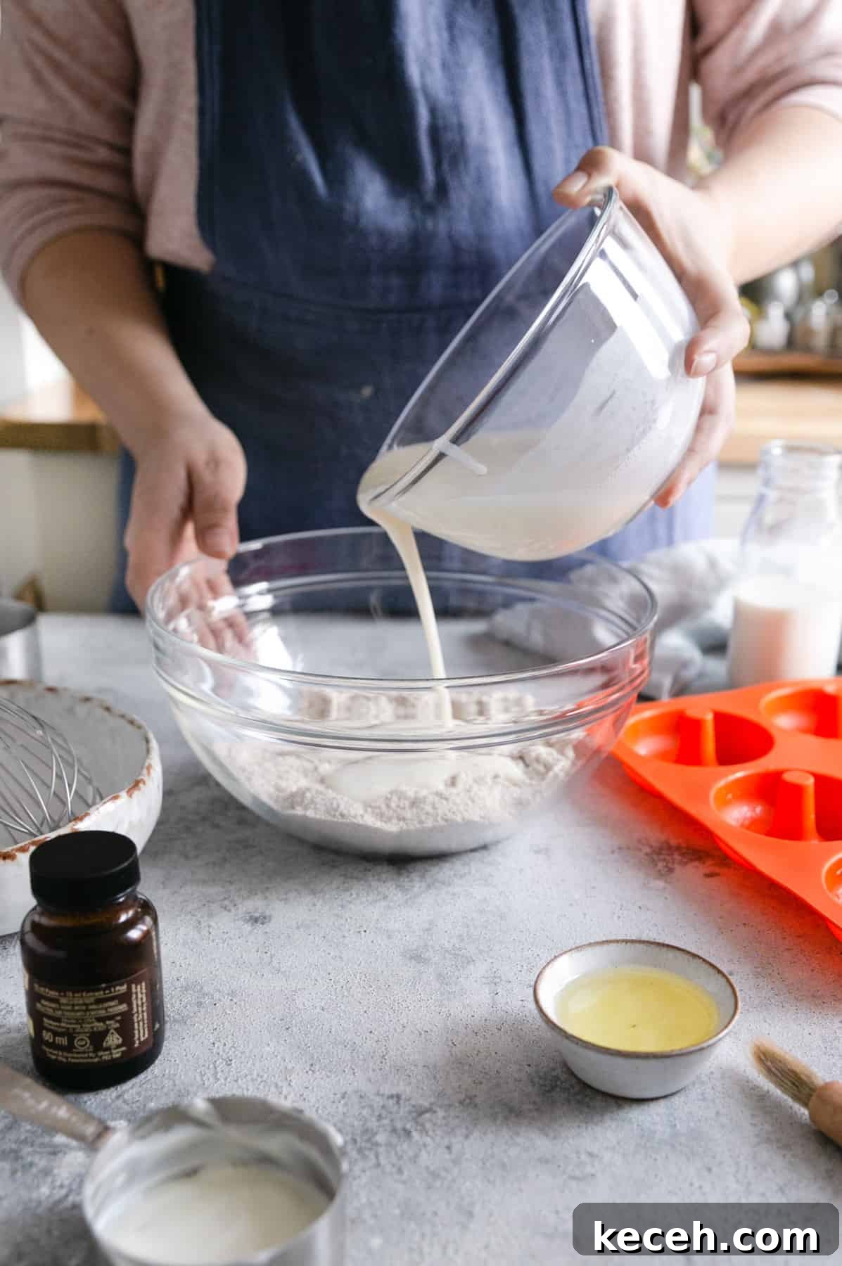 Baked Donuts with Rich Chocolate Glaze Recipe 9 a person pouring the wet ingredients into a large bowl with dry ingredients for baked doughnuts