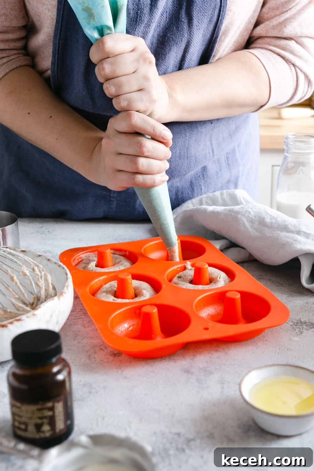 Baked Donuts with Rich Chocolate Glaze Recipe 10 a person holding a piping bag with batter for baked doughnuts, filling the silicone doughnuts mould with batter