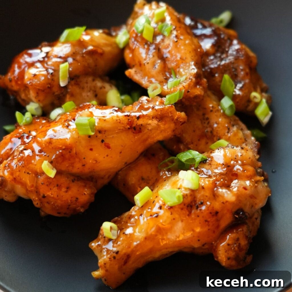 Sticky Honey Garlic Chicken Wings Recipe for Crispy Oven-Baked Wings 2 Honey Garlic chicken wings on a black bowl with chopped scallions.