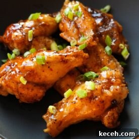 Sticky Honey Garlic Chicken Wings Recipe for Crispy Oven-Baked Wings 8 Honey Garlic Chicken Wings on a black plate with scallions on top.