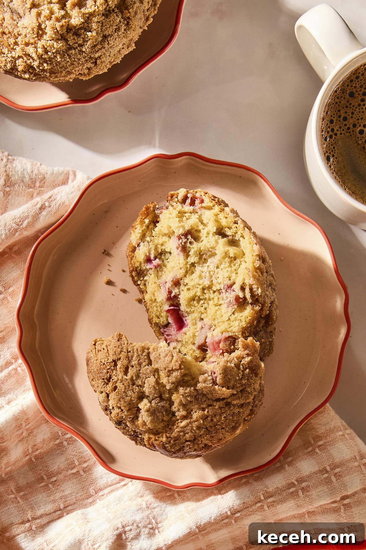 Tangy Rhubarb Muffins with Crunchy Streusel Topping 10 Plate with rhubarb muffin sliced in half with morning sunlight and cup of coffee.