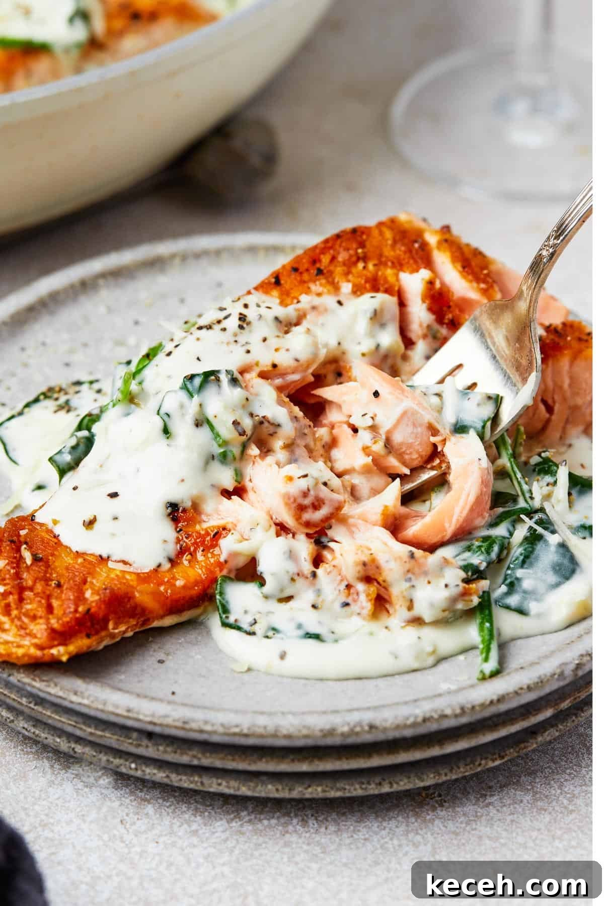 Creamy Spinach Salmon Florentine Recipe for Weeknight Dinners 11 A serving of salmon florentine. A bite of the salmon is being lifted toward the camera on a fork.