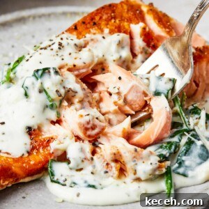 A serving of salmon florentine. A bite of the salmon is being lifted toward the camera on a fork.