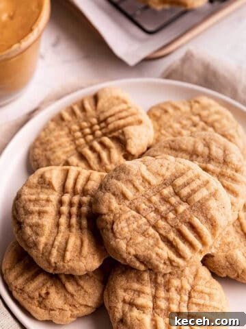 A plate of cookies with a jar of peanut butter in the back.