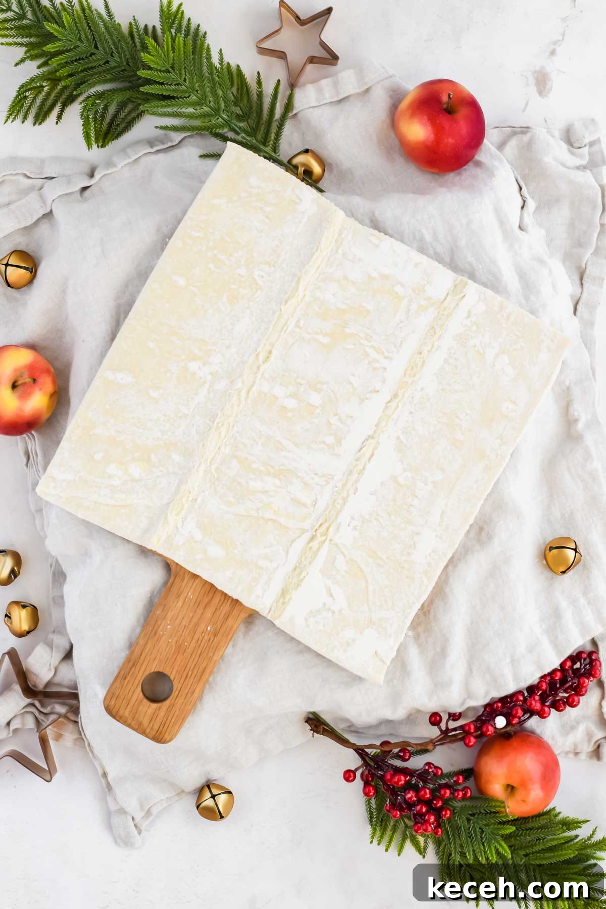 frozen puff pastry on wood cutting board surrounded by holiday decor.