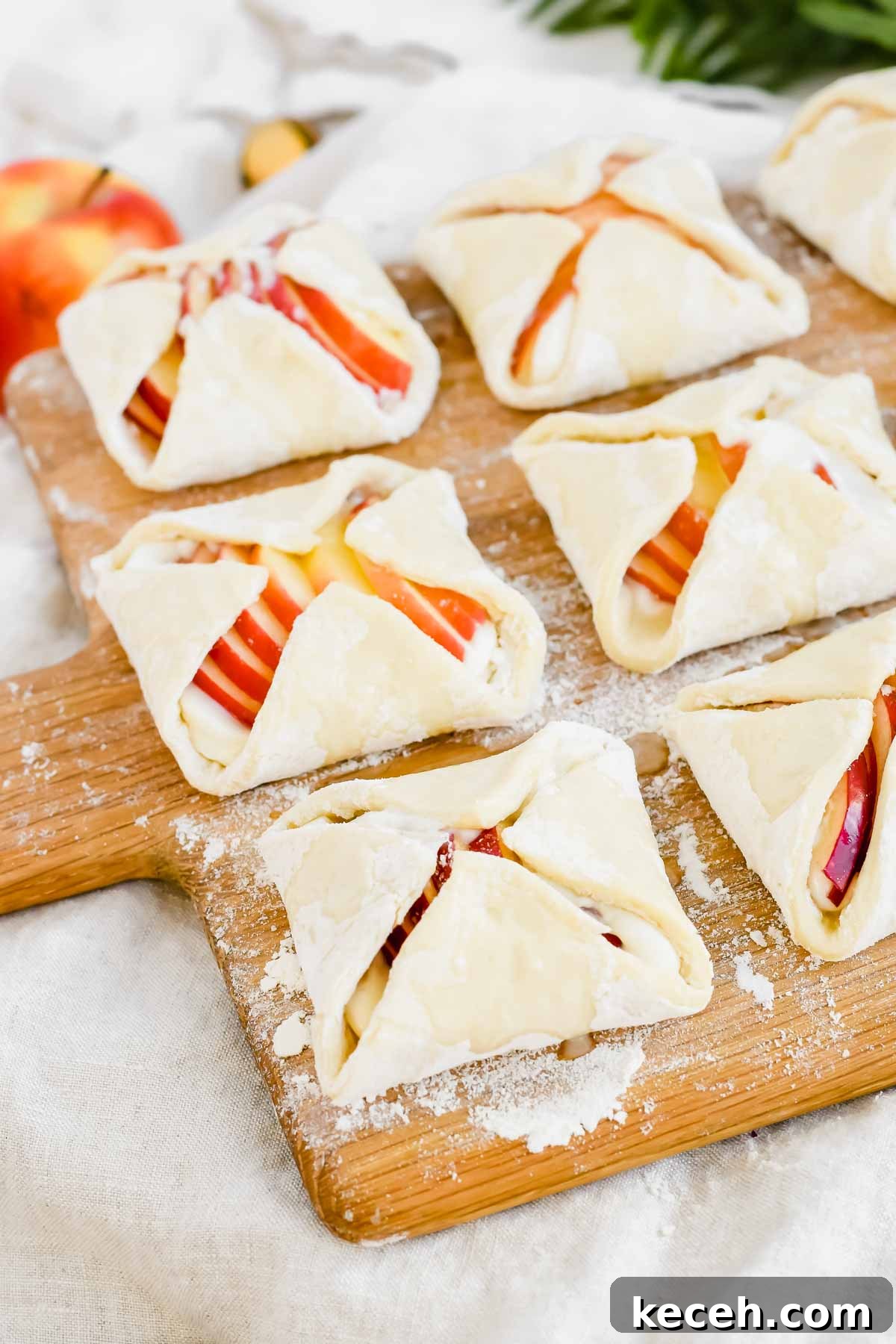 unbaked cream cheese apple danishes on wood cutting board.