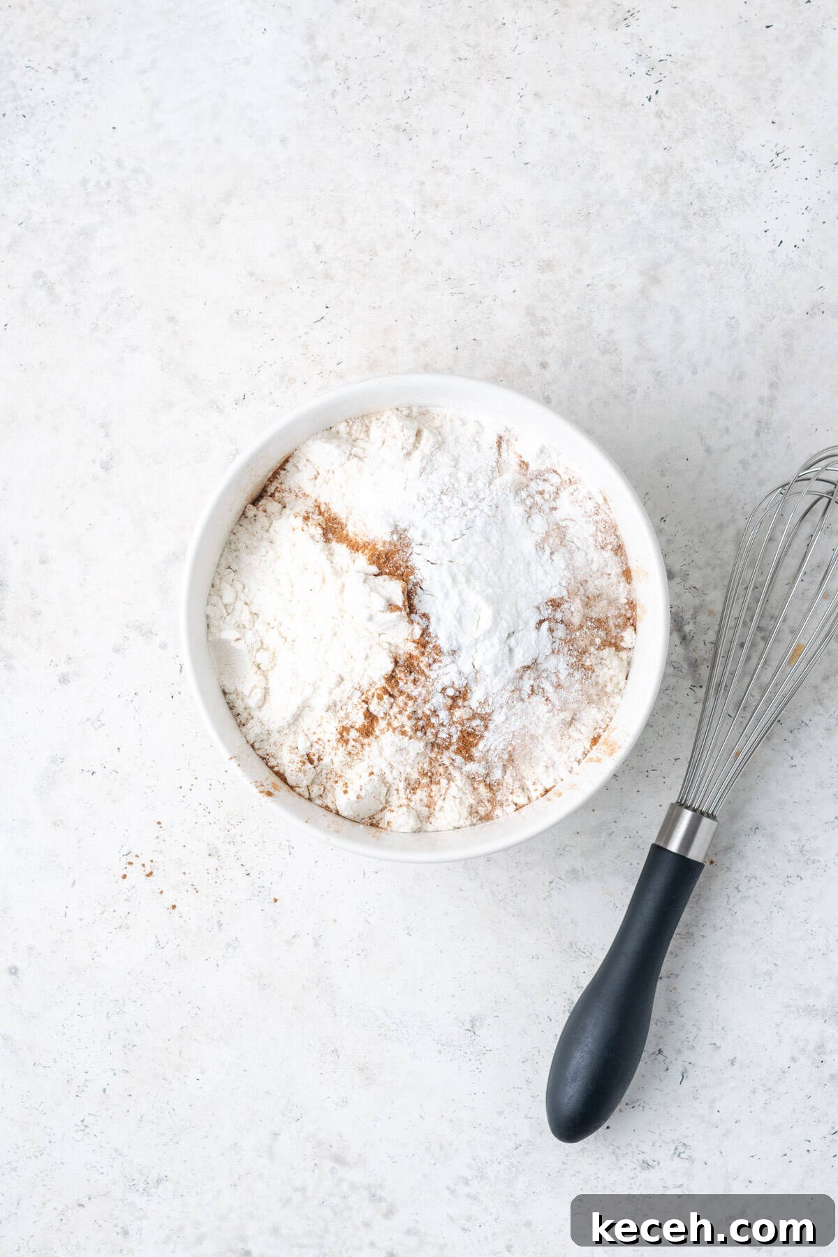 Gluten free flour, baking powder, baking soda, salt and cinnamon whisked together in a small white bowl.