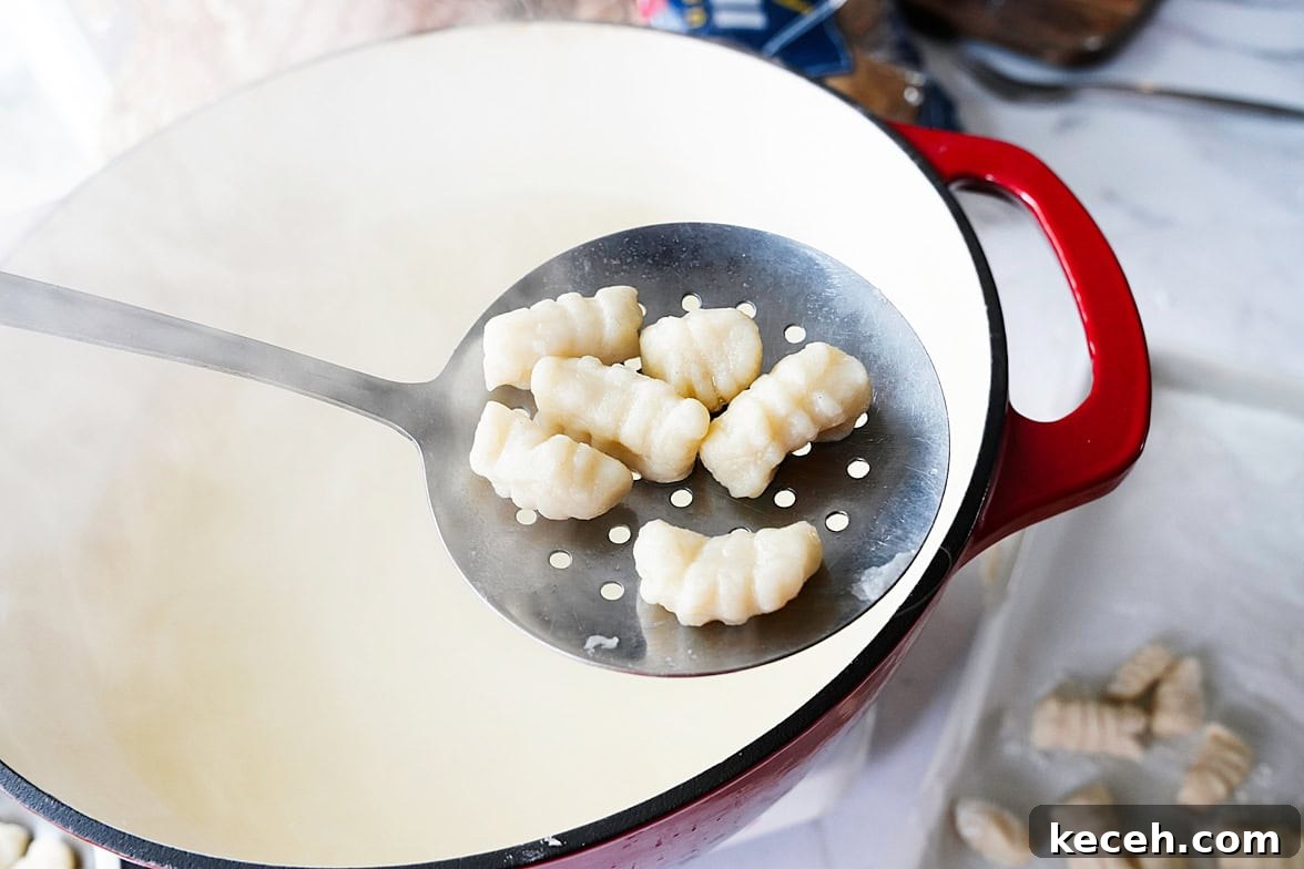 Pillowy Homemade Potato Gnocchi: Classic Italian Comfort Food 10 slotted spoon with 6 pieces of potato gnocchi after being boiled
