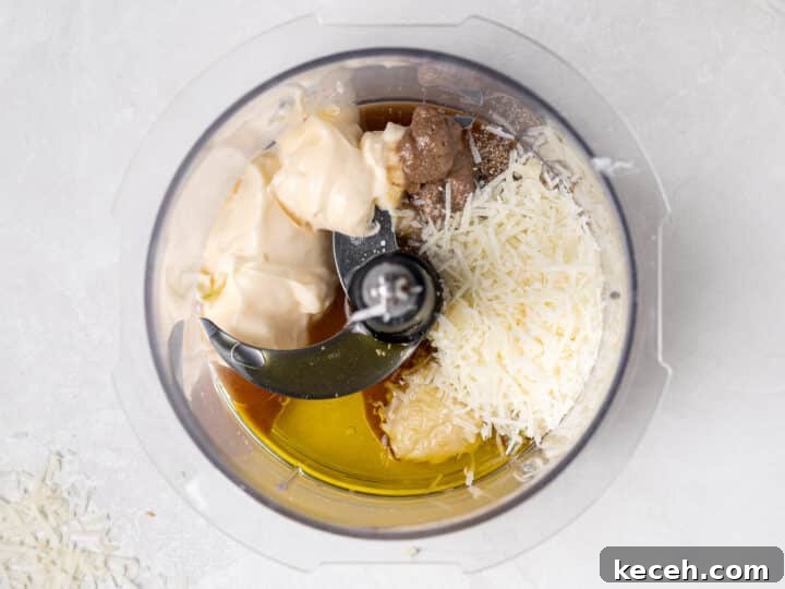 ingredients for Caesar vinaigrette in food processor including mayo, olive oil, parmesan, and anchovy paste