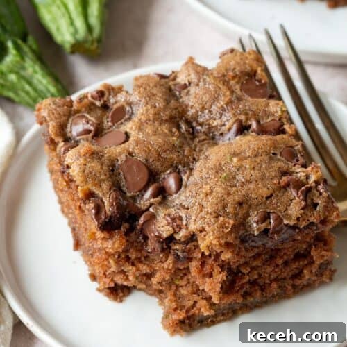 slice of chocolate chip zucchini cake with a bite taken out on a white plate.