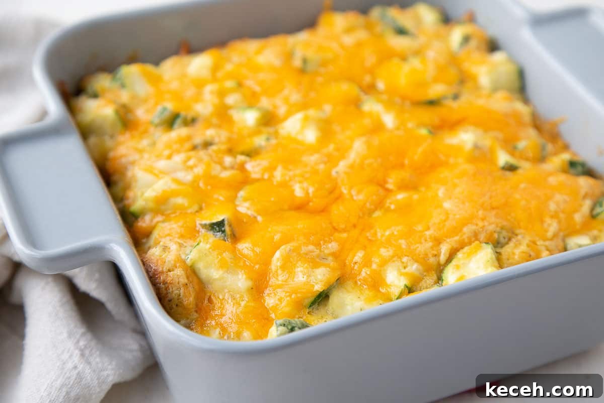 old fashioned zucchini casserole in a gray square casserole dish, topped with cheese.