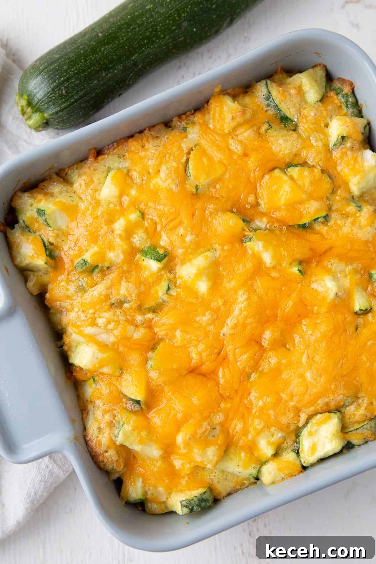 zucchini casserole topped with cheese in a gray square casserole dish.