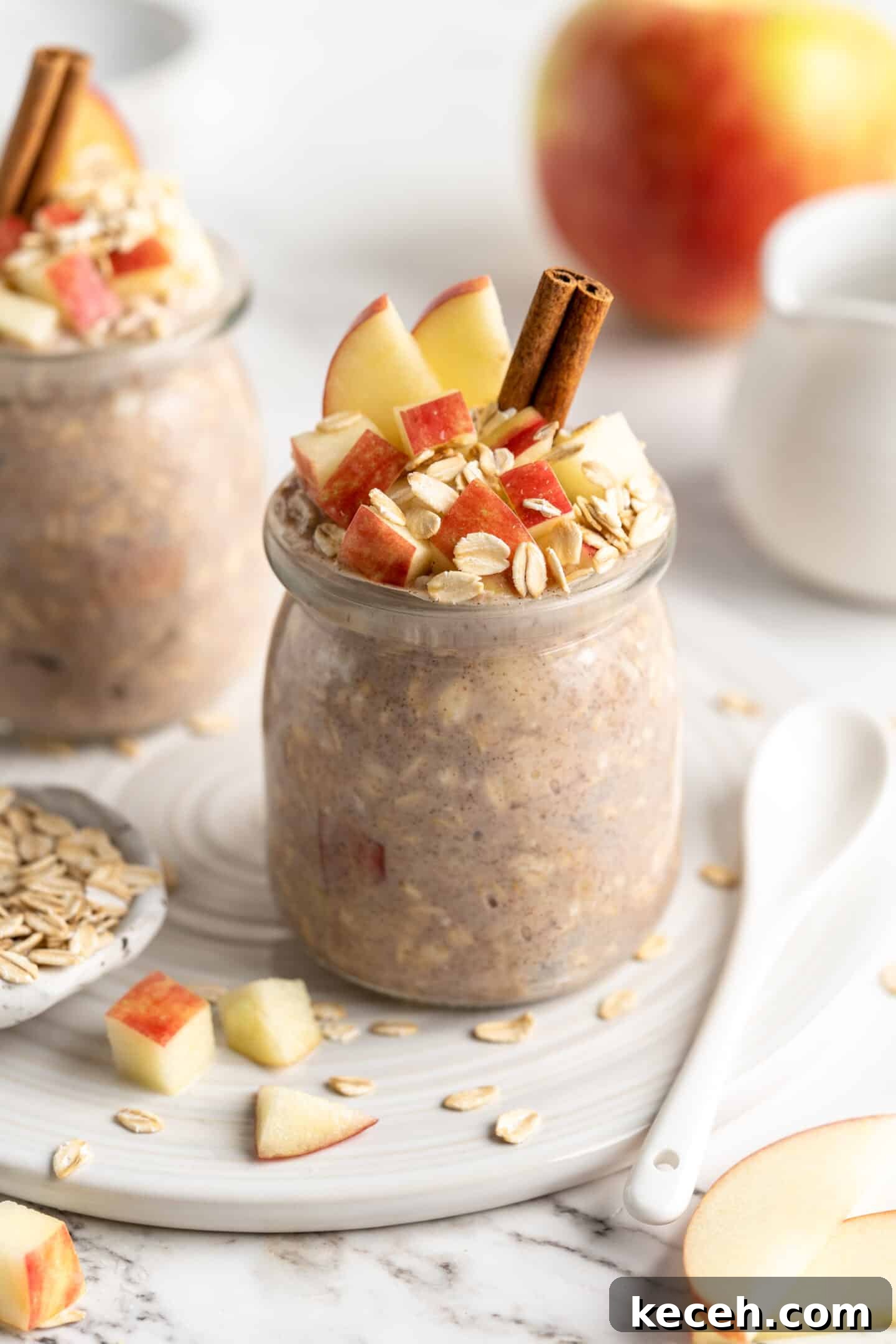 Apple pie overnight oats are packed with crisp apples, warm cinnamon, rich almond milk, and decadent maple syrup, and are an easy breakfast. two jars apple overnight oats with cinnamon sticks, oats and apples topping them, apple in background