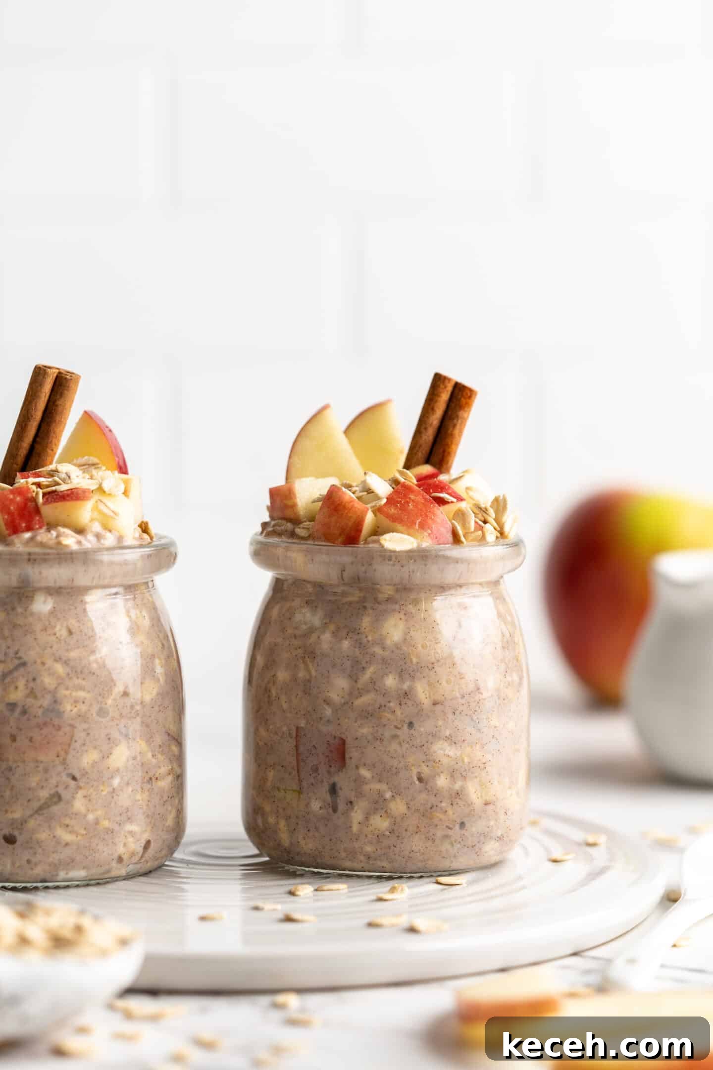 Apple pie overnight oats are packed with crisp apples, warm cinnamon, rich almond milk, and decadent maple syrup, and are an easy breakfast. two side by side jars apple overnight oats with cinnamon sticks, oats and apples topping them