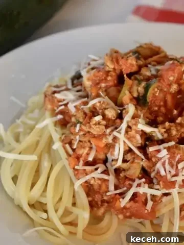Turkey Vegetable Spaghetti on a white plate with zucchini in the background.