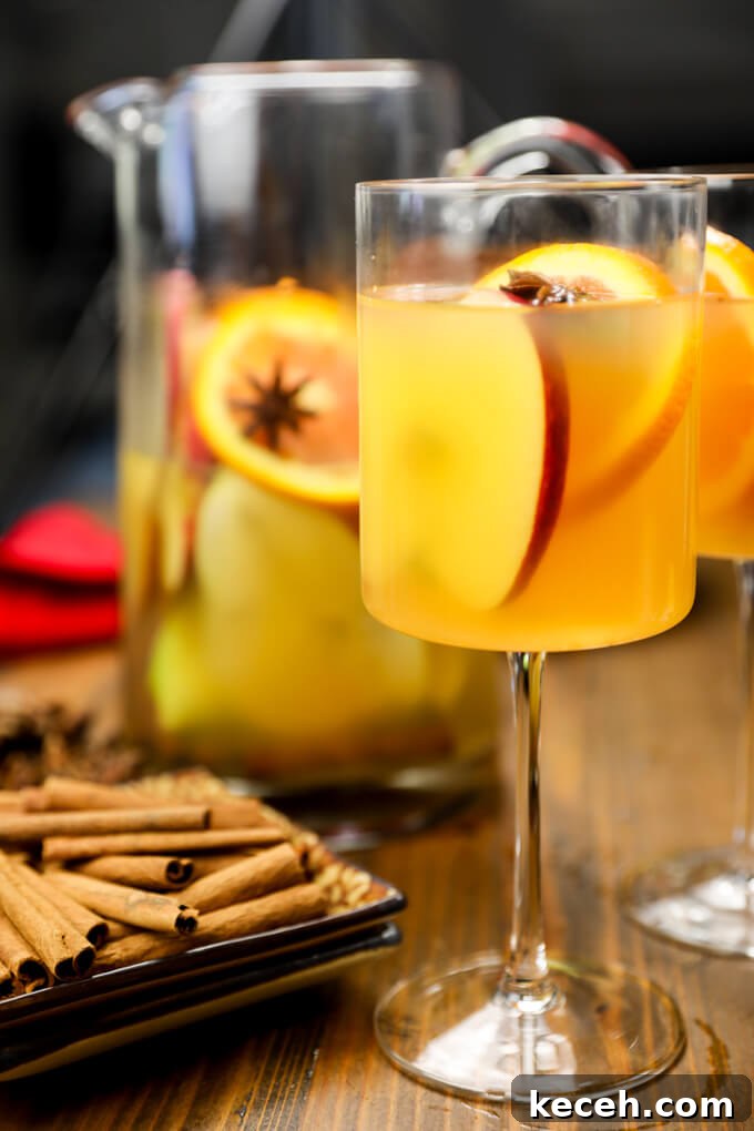 Autumn Apple Cider Sangria with Bourbon Twist 3 Two apple cider sangria cocktails with apple and orange slices. A pitcher of the same stands behind them.