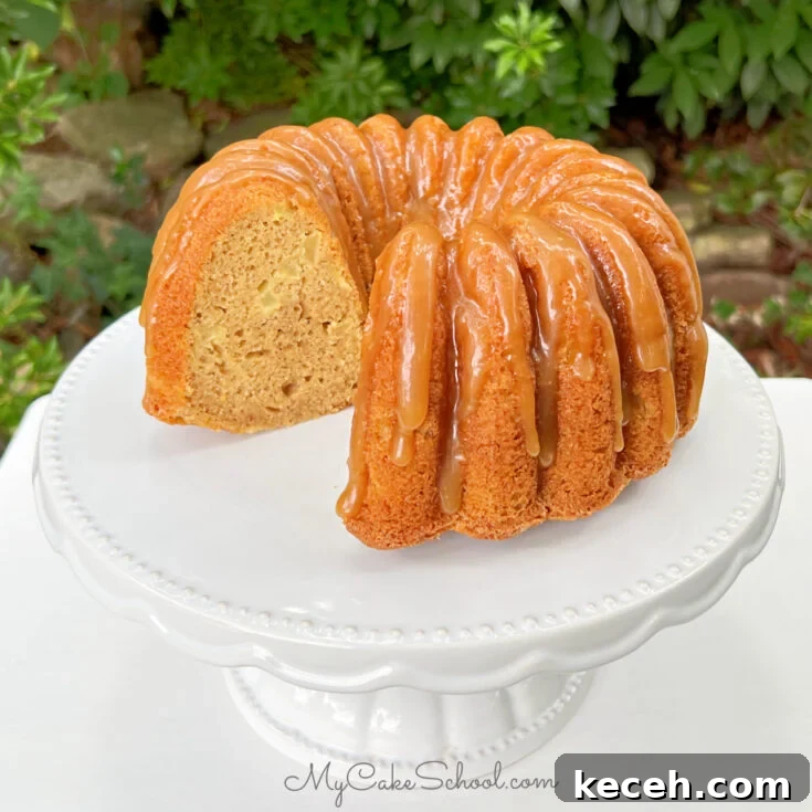 Sliced Apple Bundt Cake on white pedestal, glazed with caramel.