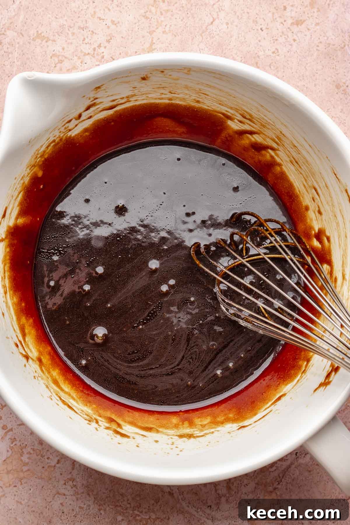 A whisk mixes wet muffin ingredients in a bowl.