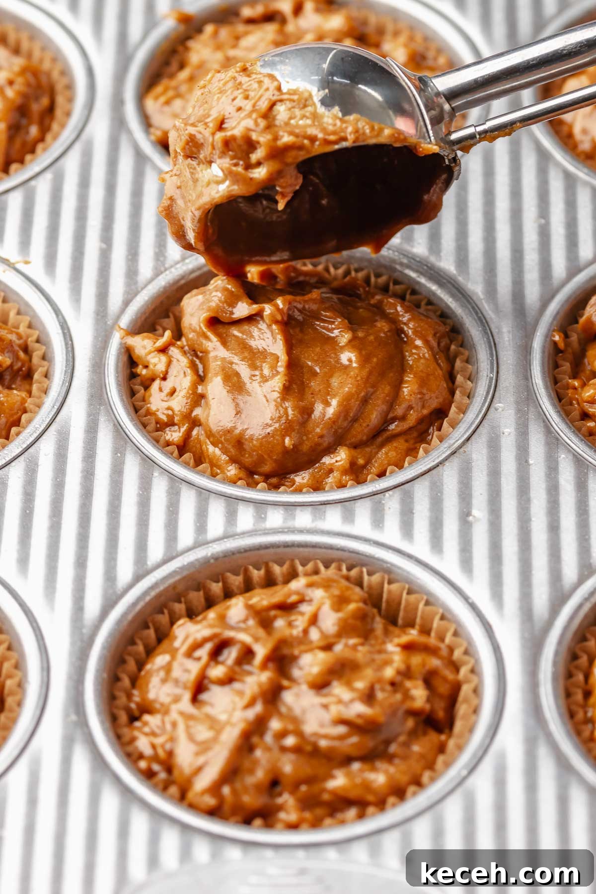 A cookie scoop adds muffin batter into a muffin tin.