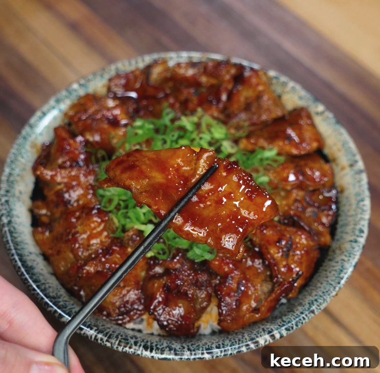 Sticky Spicy Pork Belly Recipe for Crispy Glazed Pork 3 Close-up of glazed pork belly slice held with chopsticks over a bowl of rice topped with sticky spicy pork belly and chopped scallions, showcasing the glossy sauce and juicy texture.