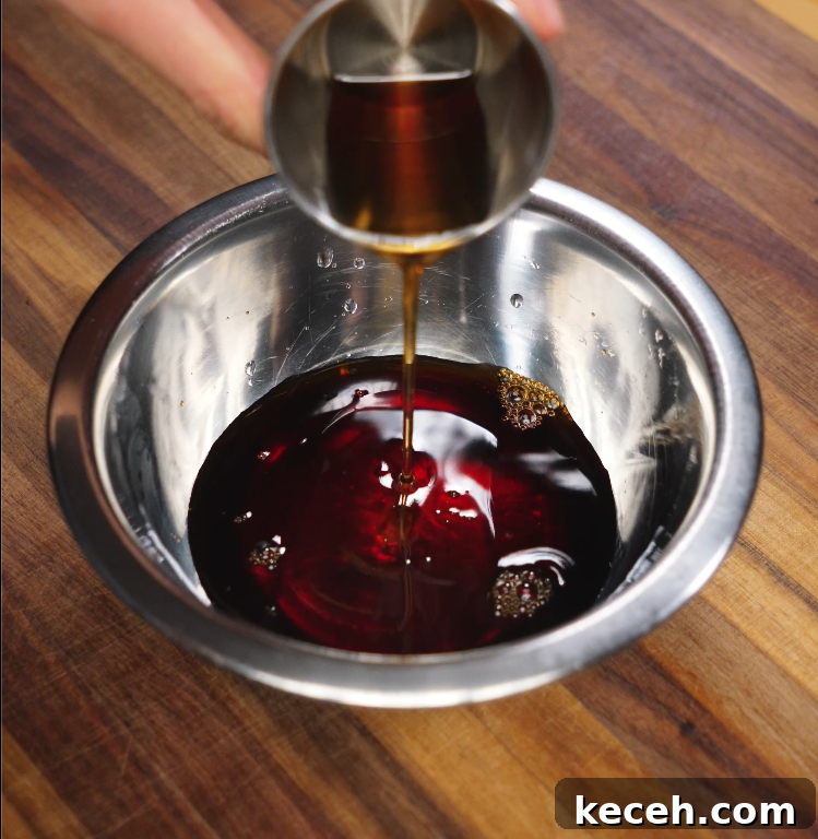 Sticky Spicy Pork Belly Recipe for Crispy Glazed Pork 4 Pouring mirin from a metal measuring cup into a bowl of marinade for pork belly, with soy sauce and other seasonings visible in a stainless steel mixing bowl.