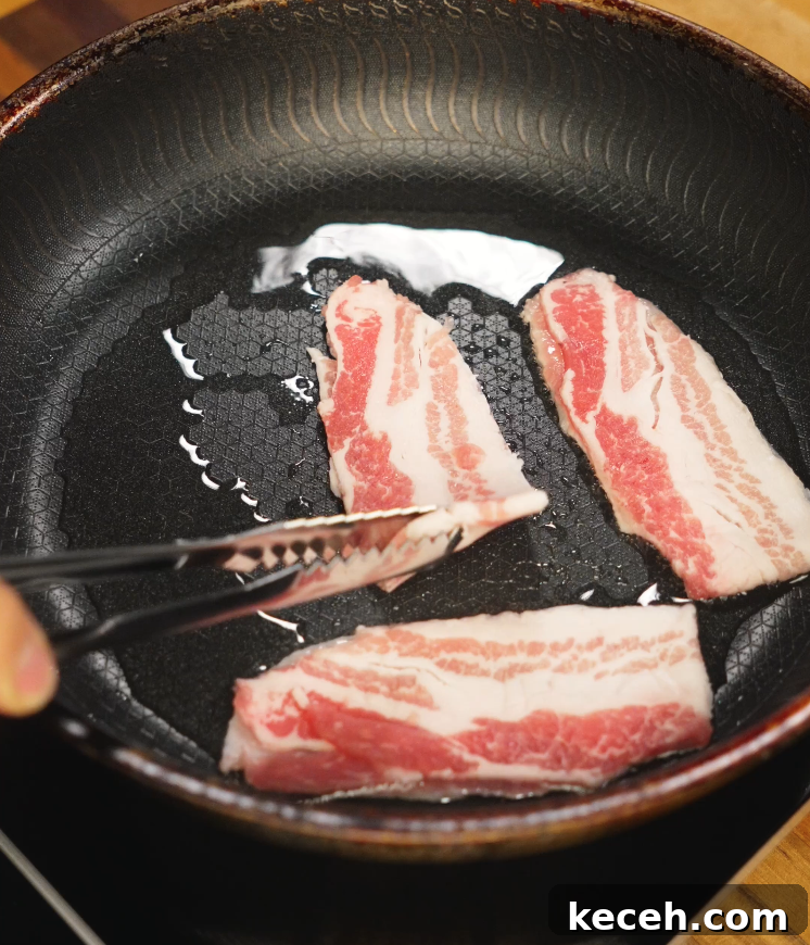 Sticky Spicy Pork Belly Recipe for Crispy Glazed Pork 5 Frying raw pork belly slices in a nonstick skillet with oil, showing the marbled layers of fat and meat beginning to render as they cook.