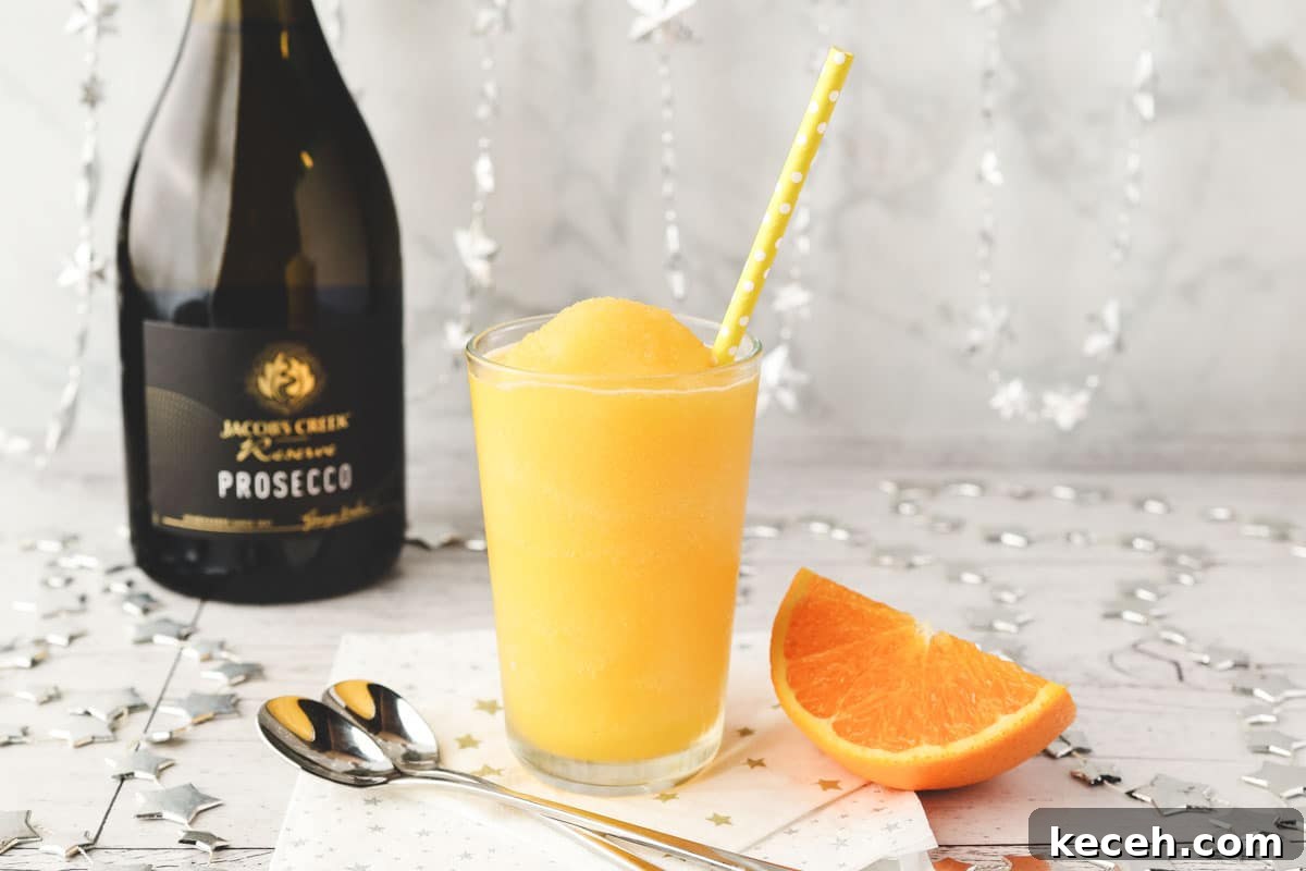 Mimosa Slushie Recipe: Sparkling Brunch Cocktail Guide 6 Glass of Mimosa slushy with tall spoons and fresh orange slice on the side.