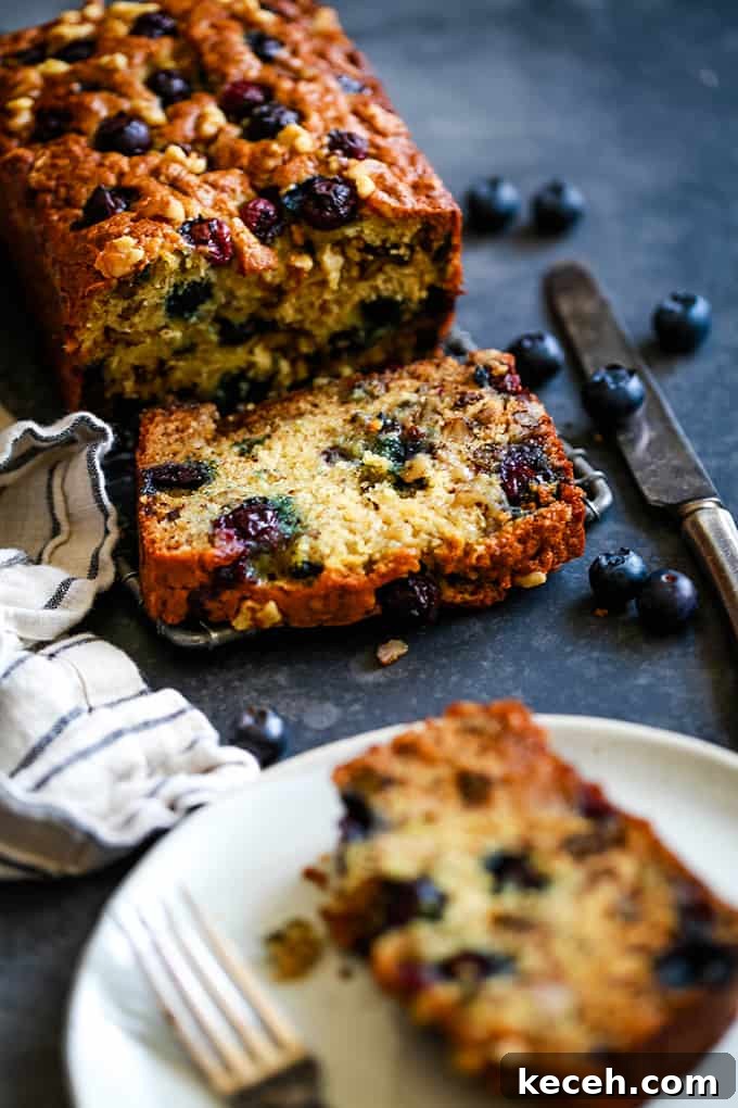 A loaf of Blueberry Walnut Banana Bread with a slice cut and a slice served on a white plate.