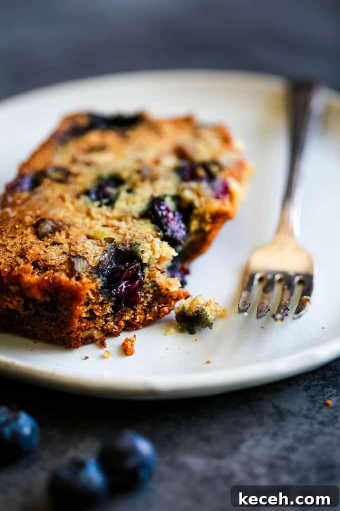 A slice of Blueberry Walnut Banana Bread on a white plate with a fork and a bite removed.