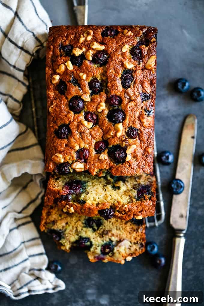 Two slices are cut from a loaf of Blueberry Walnut Banana Bread with a striped napkin and knife on either side.