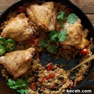 Chicken thighs with rice and black beans in a cast iron skillet, topped with cilantro and fresh jalapeños, with a gold spoon in it.