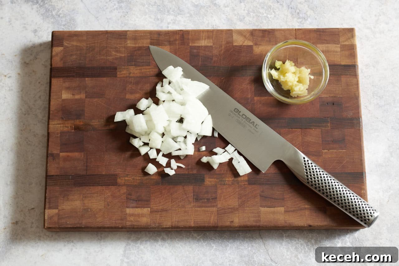 Skillet Chicken Tagine with Apricots and Warm Spices 5 A knife on a wooden cutting board with chopped onions and a small bowl of grated garlic.