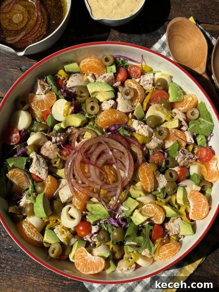 Fresh chicken salad with citrus, olives, and vegetables on a rustic wooden table.