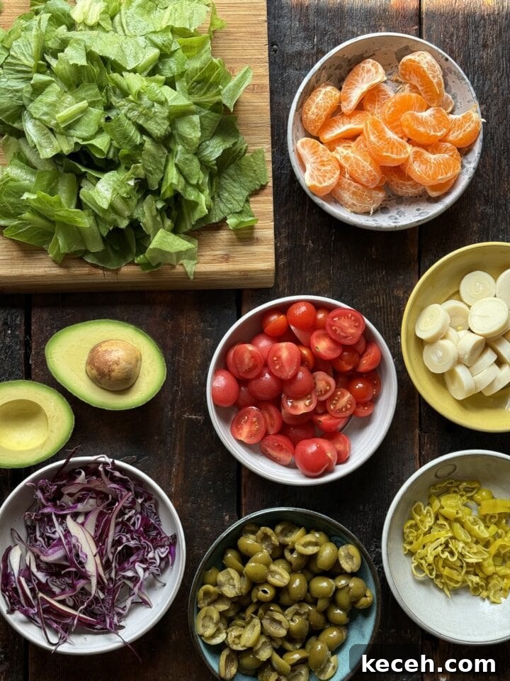 Fresh salad ingredients with lettuce, cherry tomatoes, avocado, mandarin oranges, mozzarella, green olives, red cabbage, and pickled chayote for healthy eating.