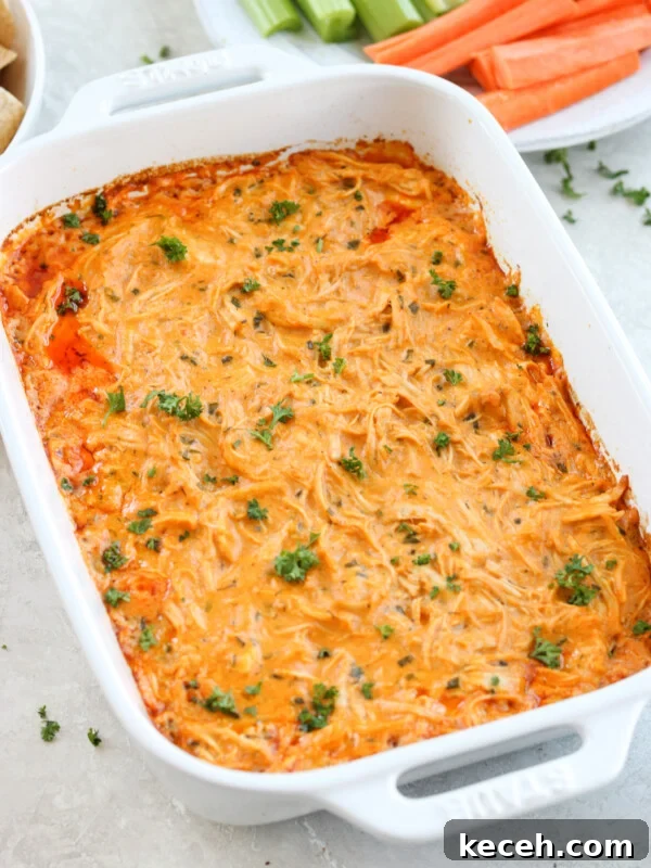 Healthy buffalo chicken dip in a white Staub baking dish topped with parsley with carrots and celery in the background